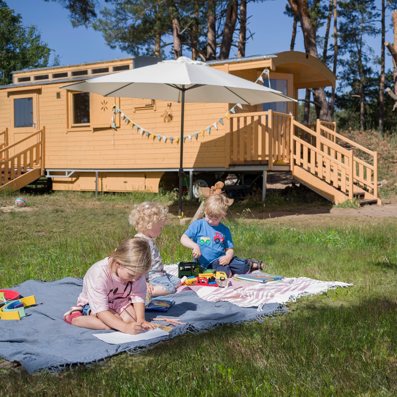 Kinder spielen auf der Wiese vor einem Bauwagen, der einem Waldkindergarten gehört.