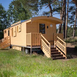 Bauwagen steht im Sommer auf einer Wiese unter Bäumen und sieht aus wie ein Kindertraum von einer Schutzhütte