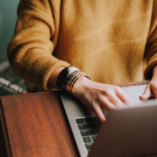 Eine Person sitzt an einem Schreibtisch und tippt auf einem Laptop.