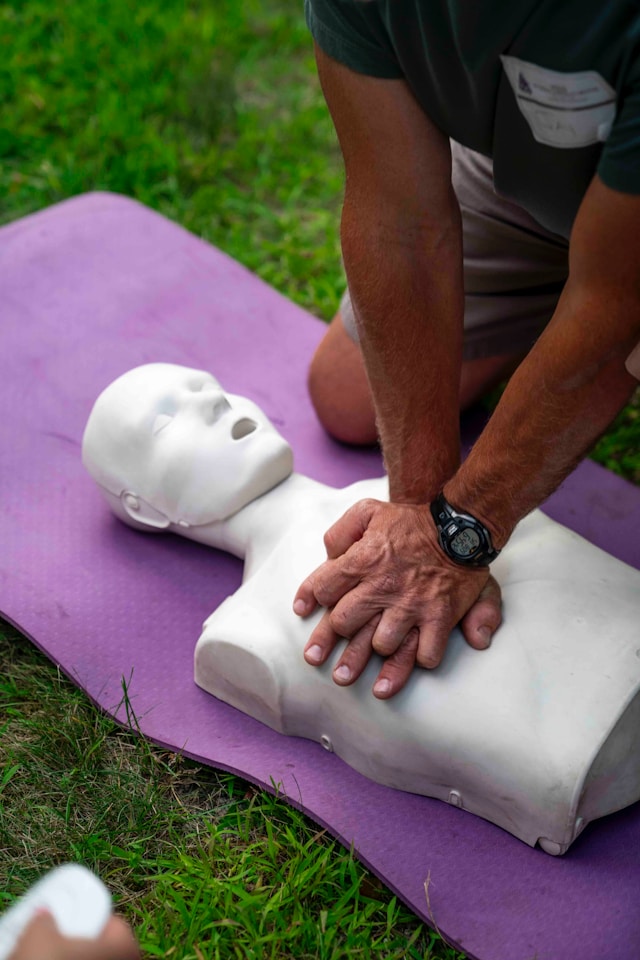 Eine Person gibt einer Puppe eine Herz-Druck-Massage auf einer Wiese.