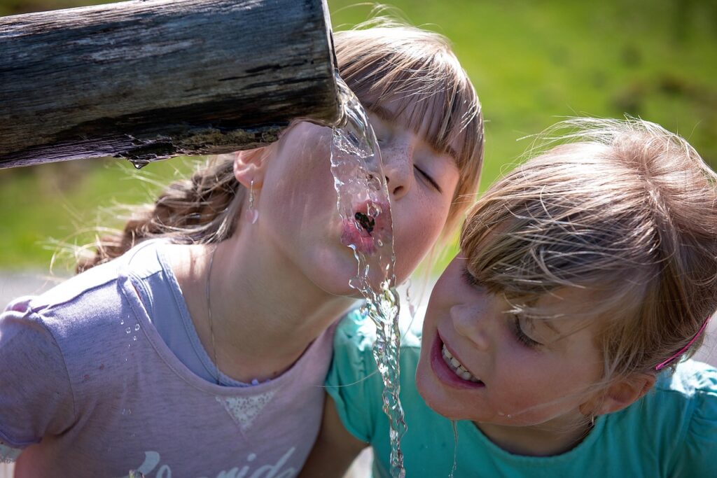 Kinder trinken Wasser aus einem Trinkbrunnen.