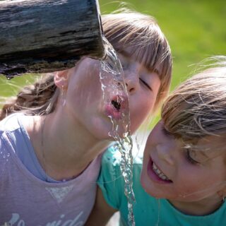 Kinder trinken Wasser aus einem Trinkbrunnen.