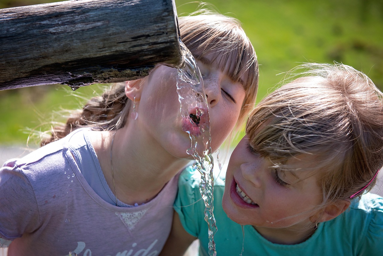 Kinder trinken Wasser aus einem Trinkbrunnen.